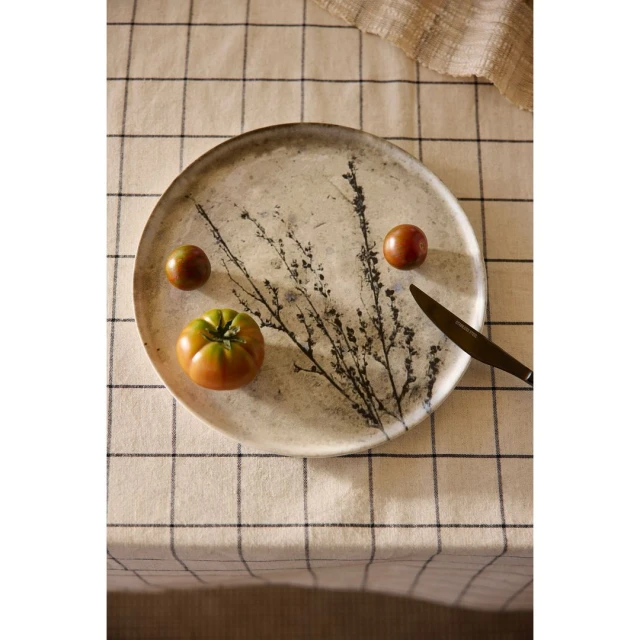 Overhead shot of heirloom tomatoes and a knife arranged on a decorative plate with a branch design over a checkered tablecloth.