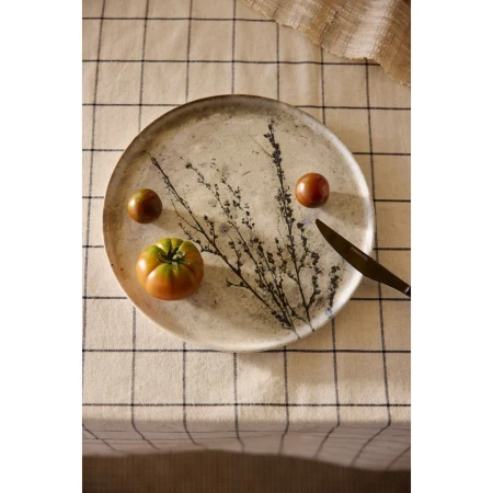 Overhead shot of heirloom tomatoes and a knife arranged on a decorative plate with a branch design over a checkered tablecloth.