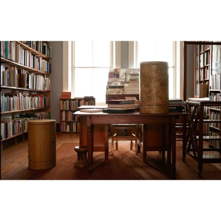 Interior of a library with wooden tables, chairs, bookcases filled with books, and natural light streaming through the windows.