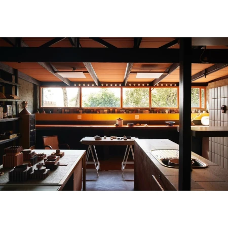 Indoor shot of a sparsely decorated home interior featuring a work table with objects, a sink, and a window overlooking green trees.
