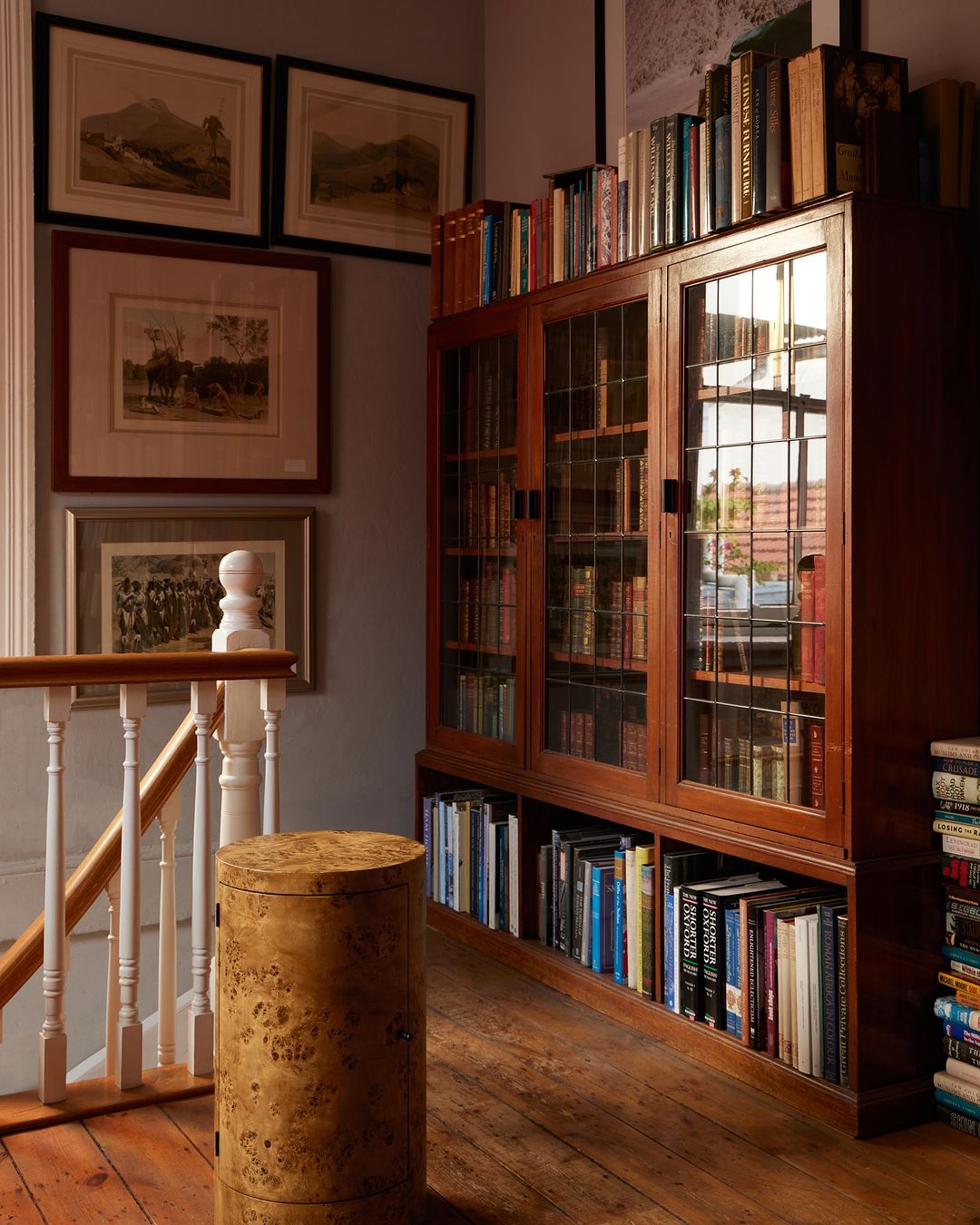 Home library featuring a wooden bookcase filled with books, a cylindrical table, framed art on the wall, and a white banister.