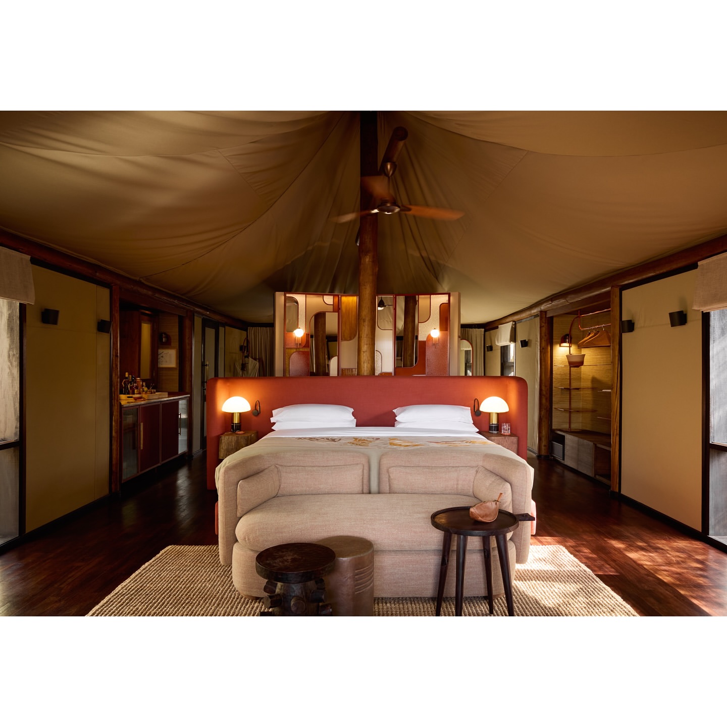 Inside a luxury tented room featuring a large bed with a sofa, lamps, and a decorative screen, offering a cozy and elegant retreat.