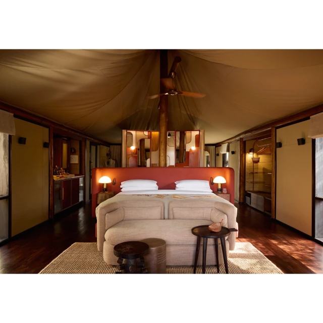Inside a luxury tented room featuring a large bed with a sofa, lamps, and a decorative screen, offering a cozy and elegant retreat.