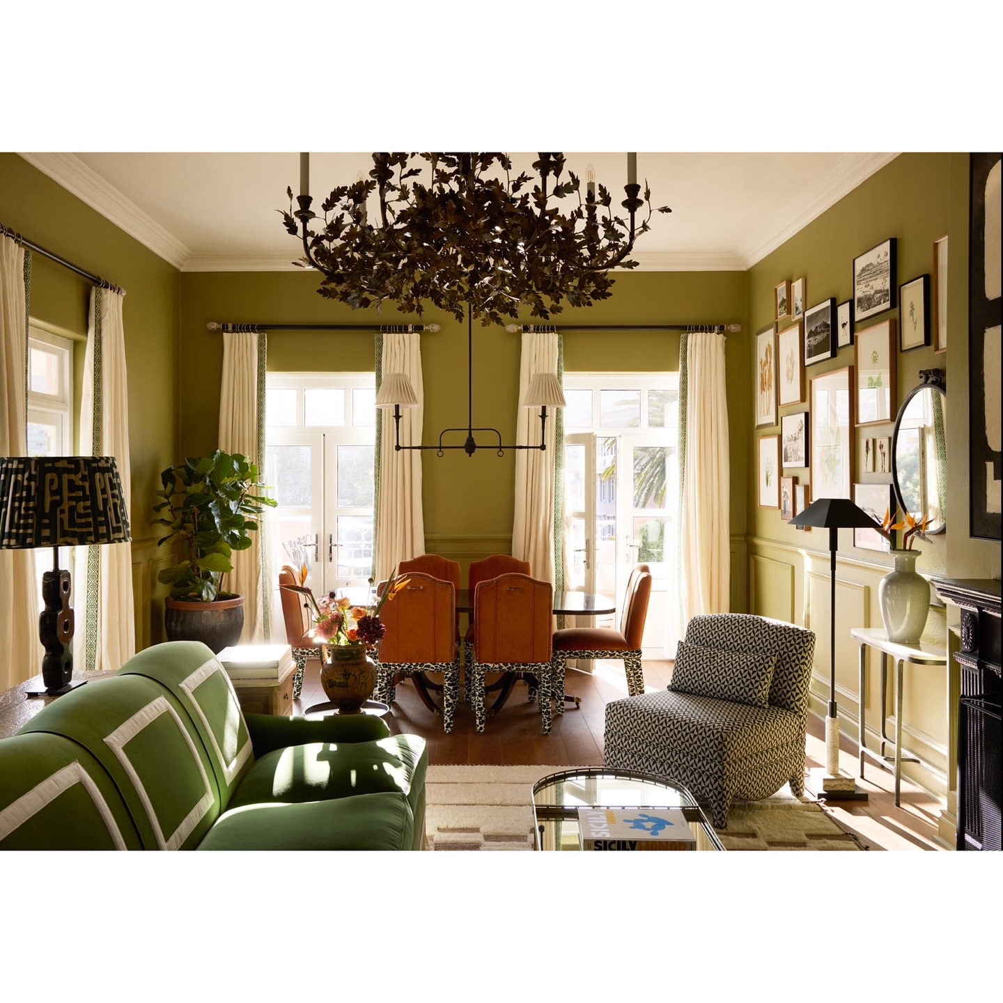 Living room and dining area of an opulent home interior with green walls, stylish furniture, and a modern chandelier centerpiece.