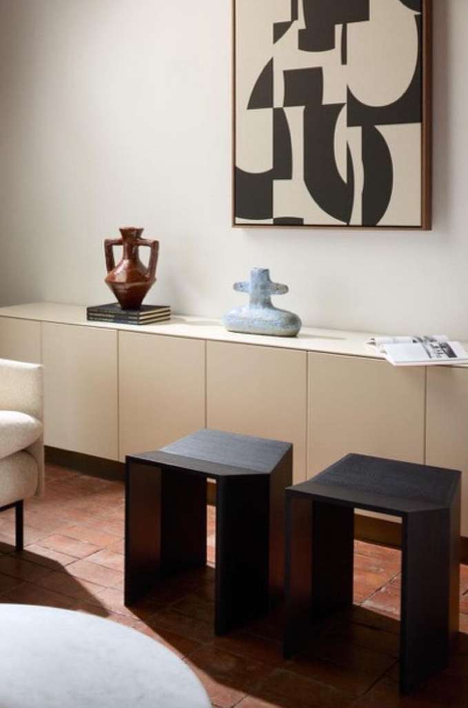 Interior view showcasing a modern living room with two dark brown side tables, art objects on a cabinet, and a geometric artwork.