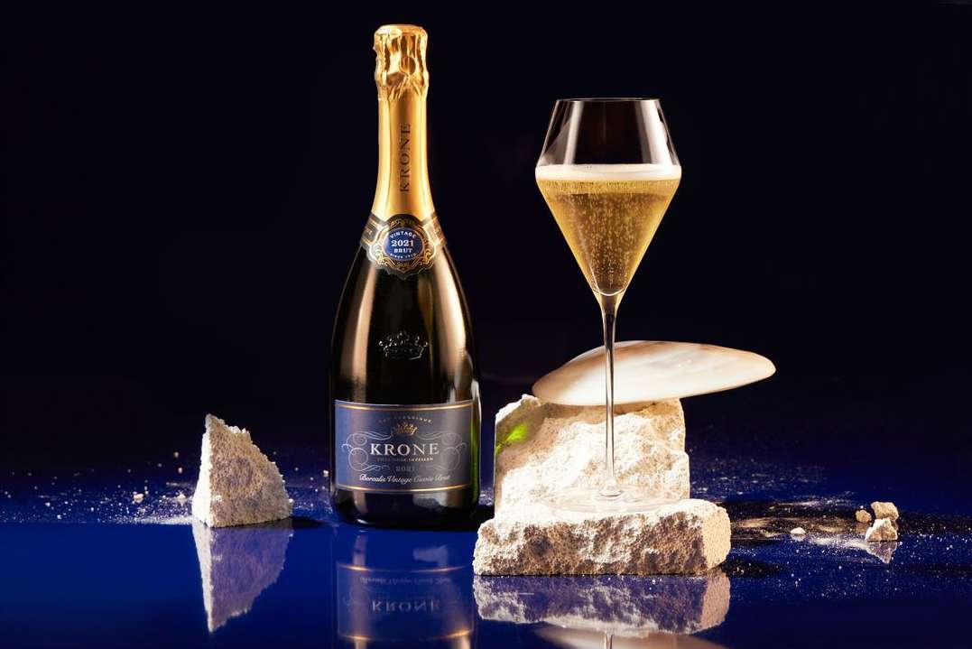 Still life composition: a bottle of sparkling wine, a filled glass, and decorative stone elements against a dark blue backdrop.