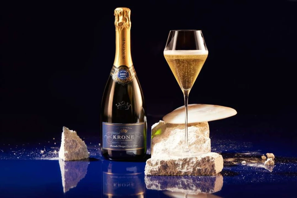Still life composition: a bottle of sparkling wine, a filled glass, and decorative stone elements against a dark blue backdrop.