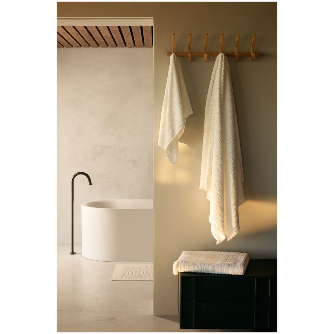 Interior of a modern bathroom featuring a white bathtub, black faucet, and light-colored walls, with a towel rack holding soft, white towels.