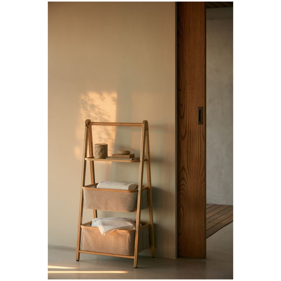 Bathroom interior with wooden shelf ladder featuring storage baskets and towels, set against a cream-colored wall and wooden door frame.