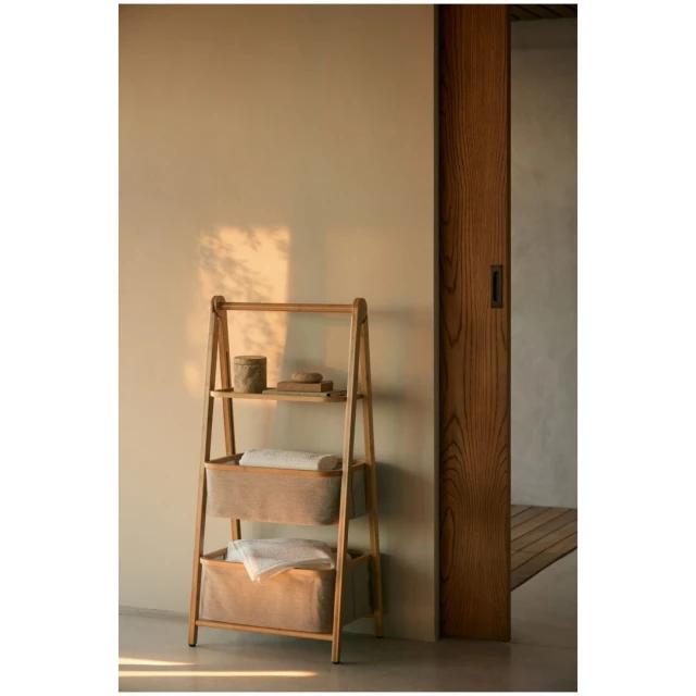 Bathroom interior with wooden shelf ladder featuring storage baskets and towels, set against a cream-colored wall and wooden door frame.