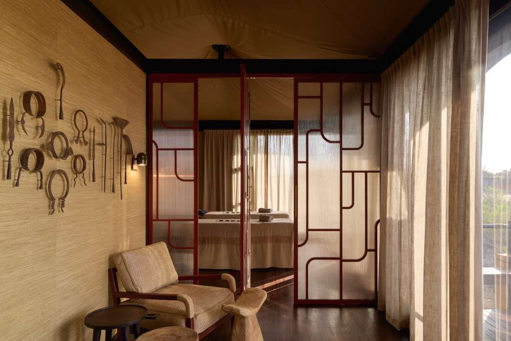 Interior view of a spa room with armchairs, a massage table visible through a patterned divider, and decorative metalwork on the wall.