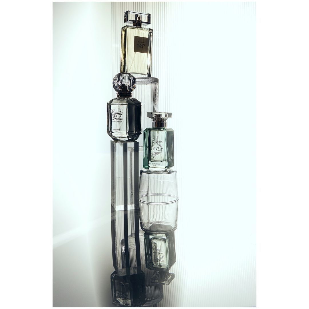 Stack of perfume bottles on reflective surface featuring clear and geometric shapes, creating minimalist and modern aesthetic.