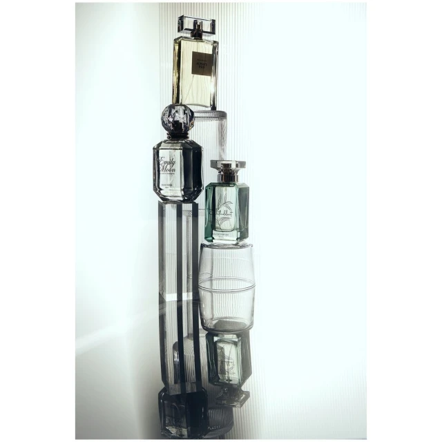 Stack of perfume bottles on reflective surface featuring clear and geometric shapes, creating minimalist and modern aesthetic.