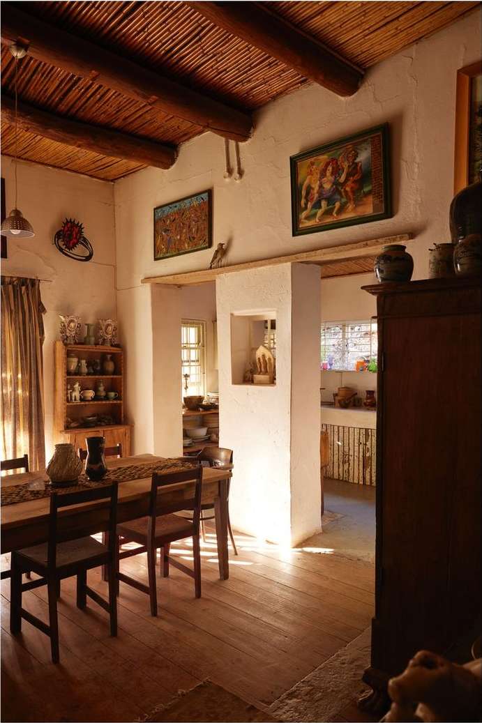 Rustic dining room with wooden table and chairs, pottery, artwork, and a traditional thatched roof. Warm, inviting interior.