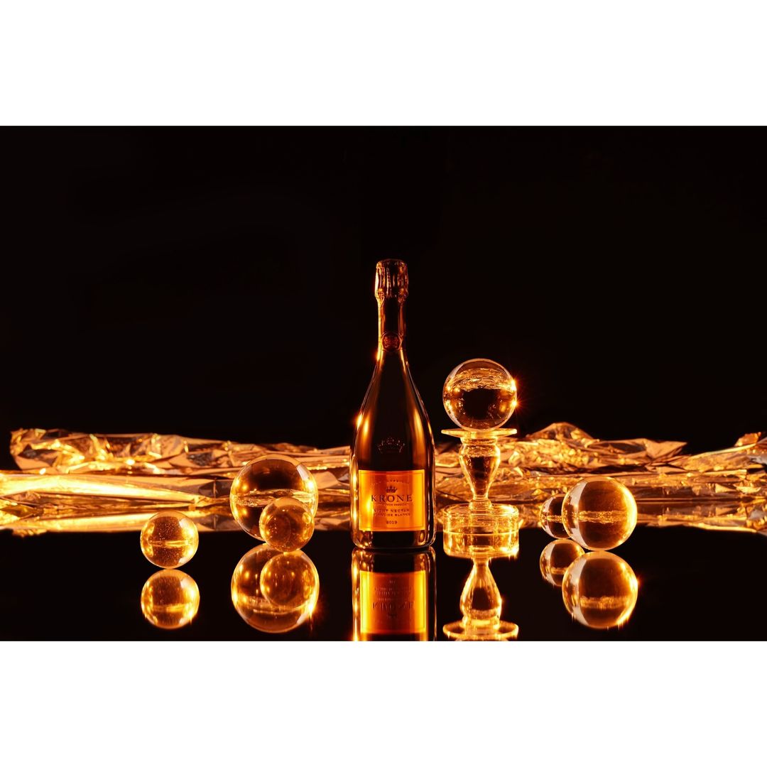 Bottle of champagne with crystal balls on reflective surface against black backdrop. Festive, celebration-themed product photography.