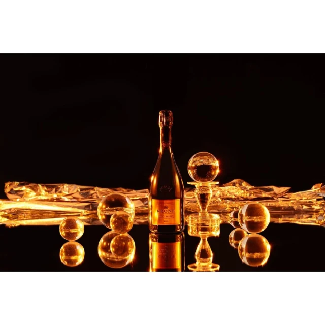 Bottle of champagne with crystal balls on reflective surface against black backdrop. Festive, celebration-themed product photography.
