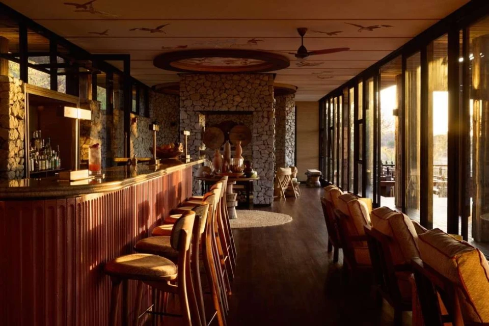 Interior of a hotel bar lounge area with stone walls, a bar with high chairs, tables with decorative items, and comfortable seating.