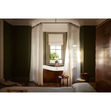 Interior view of a spa treatment room with a copper tub, round wood tables, sheer curtains, and dark green walls.