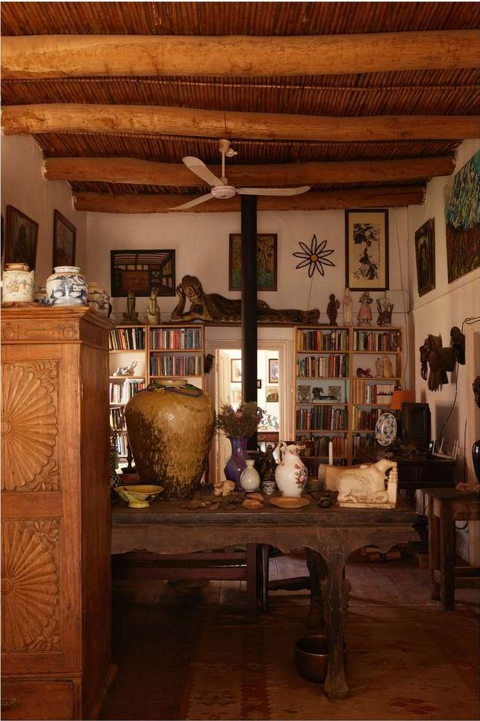 Interior view showcases a wooden table adorned with pottery and ceramics in a room filled with books and an eclectic mix of decor.