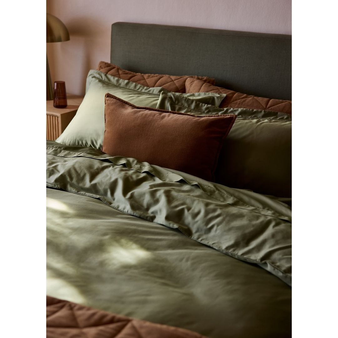 Olive green bedding ensemble with pillows and duvet cover. Home interior decor featuring soft textures and warm lighting.