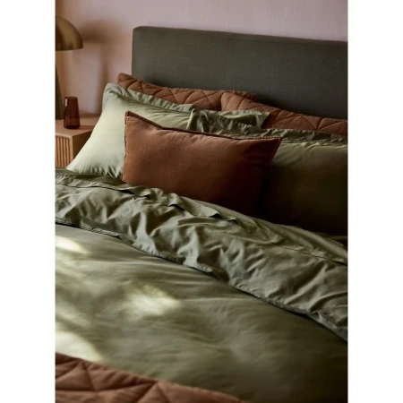 Olive green bedding ensemble with pillows and duvet cover. Home interior decor featuring soft textures and warm lighting.