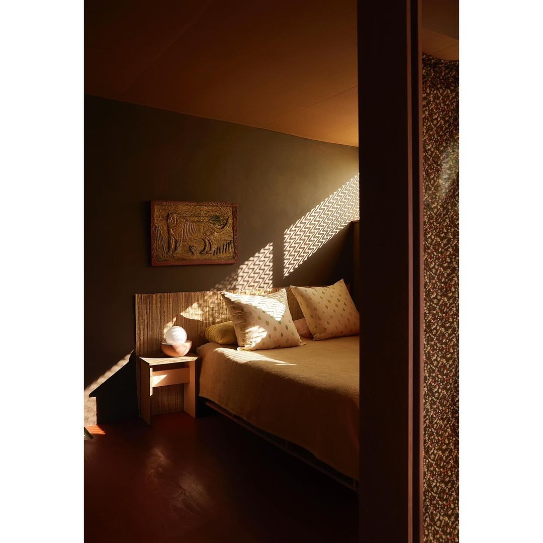 Bedroom interior with a neutral palette featuring a bed with patterned pillows, a wooden nightstand, and natural light filtering through a window.