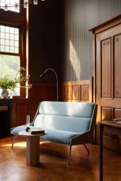Light blue upholstered sofa with metal legs placed in a wood-paneled interior with herringbone parquet flooring and tall windows.