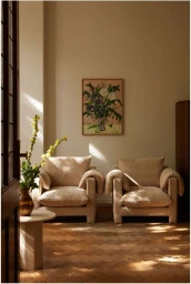 Two beige armchairs on a herringbone wooden floor with a floral painting on the wall captured by Inge Prins.