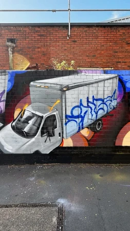 Graffiti art on a brick wall features a semi-truck with detailed shading and blue accents, complemented by abstract backgrounds.