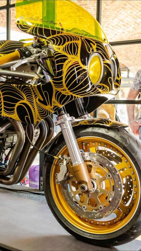 A close-up of a black and yellow custom motorcycle with intricate line details and a gold rimmed tire fills the frame.