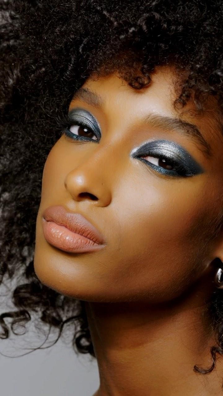 Close-up of a young adult Black woman with textured hair and smoky eyeshadow posing in a photo studio.
