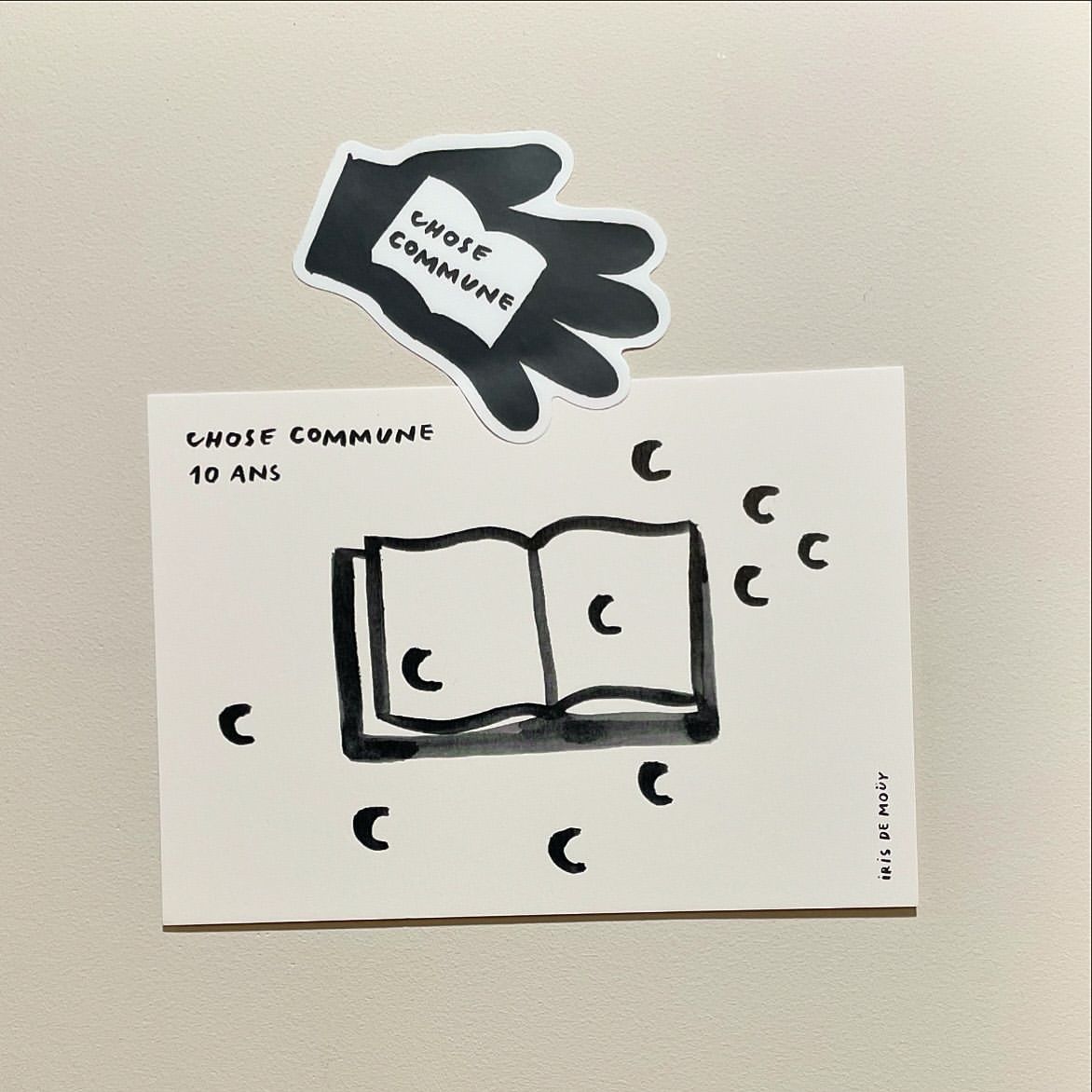 Illustrated book on a white background, accompanied by a hand-shaped black and white sticker holding a miniature book, simple line drawing art.