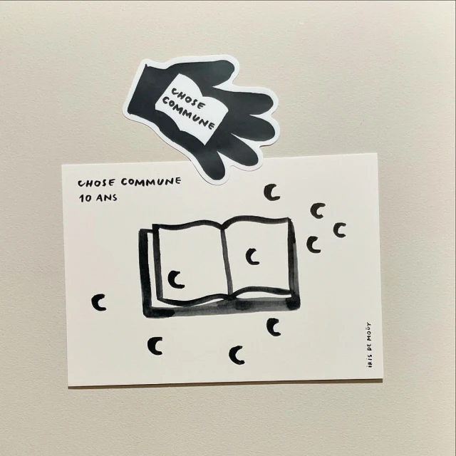 Illustrated book on a white background, accompanied by a hand-shaped black and white sticker holding a miniature book, simple line drawing art.