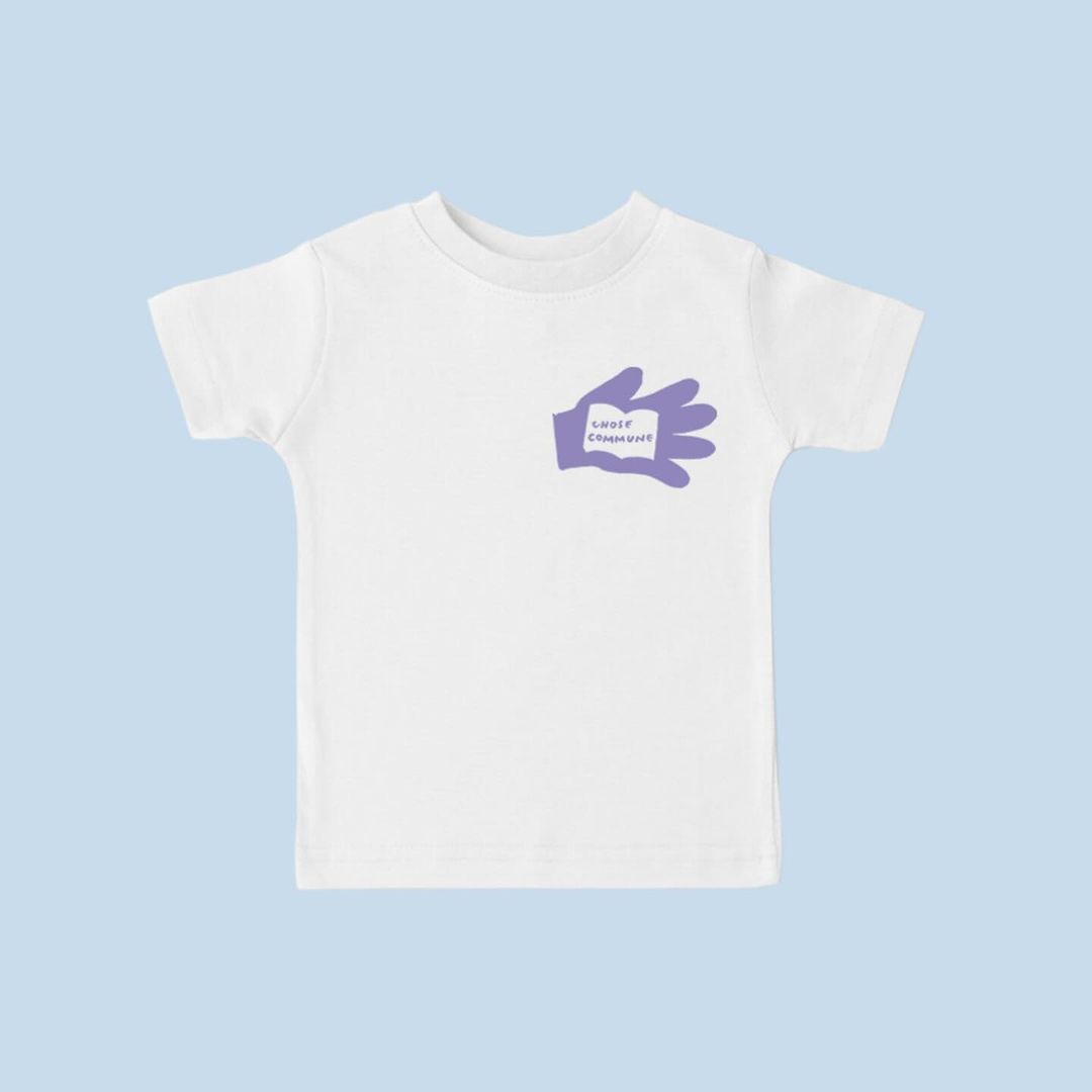 White toddler t-shirt features a graphic of a purple hand holding a small sign with the text 'Gooey Champions' against a light blue background.