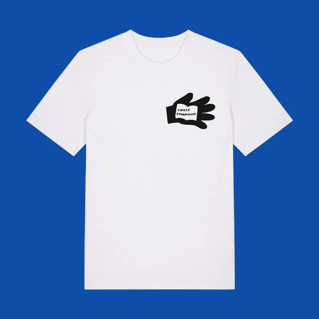 White t-shirt with a black graphic design of a hand holding a piece of paper with the words 'SHOES COMMUNE' printed on it.