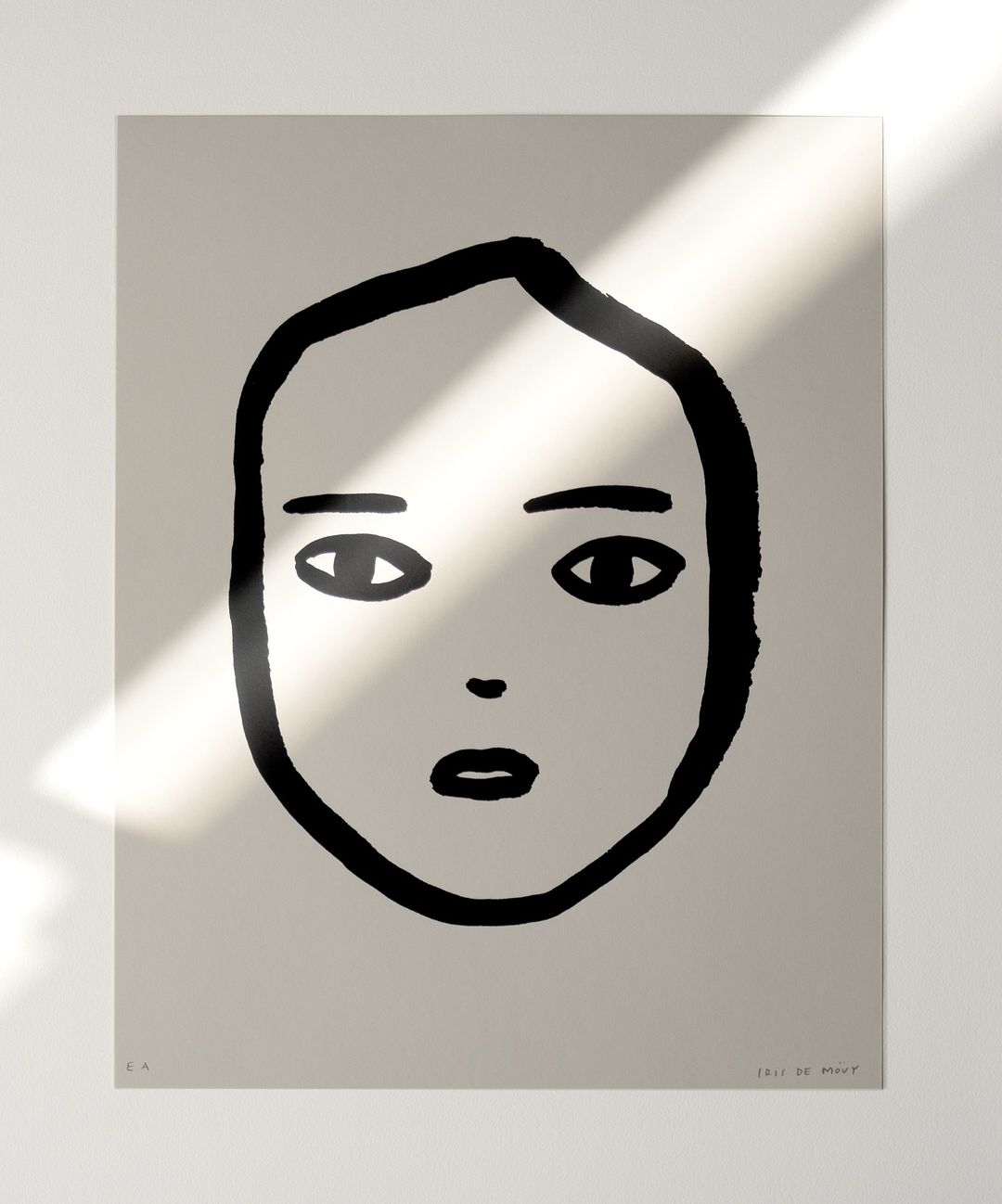 Black and white art print of a simple face with bold lines, set against a neutral background with soft light creating shadows.