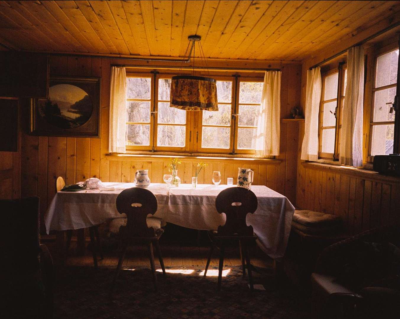 Cozy dining room interior with wooden walls, a table set for a meal, and natural light streaming through the windows.