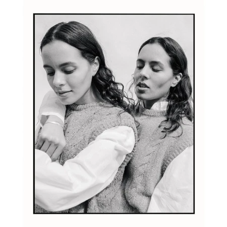 Monochromatic portrait of two women with curly brown hair wearing matching sweaters and white shirts in a close-up studio shot.