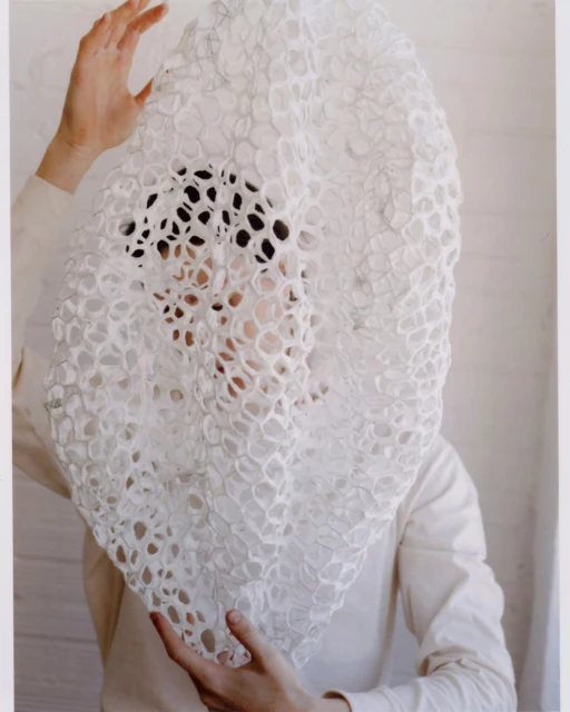 Person holding a large, textured white textile in front of their face, obscuring the view, creating an abstract and intriguing visual.