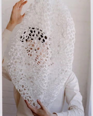 Person holding a large, textured white textile in front of their face, obscuring the view, creating an abstract and intriguing visual.