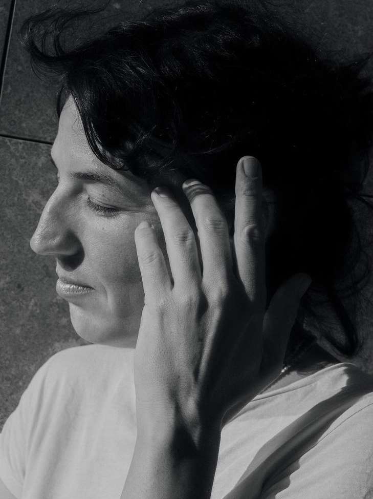 Close-up portrait of a woman with dark hair touching her face, captured in monochrome by photographer Iris Humm.