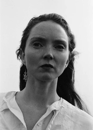Monochrome portrait of a woman wearing a white collared shirt and hanging drop earrings against a plain sky background.