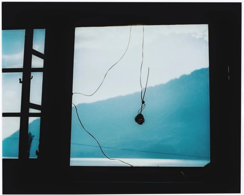 Window view of a mountain and lake with a hanging string and knot inside a darkened room, creating a contemplative atmosphere.