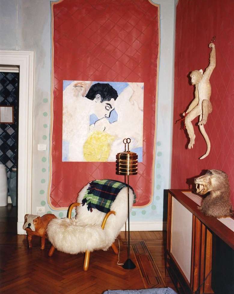 Living room interior with a furry chair, modern floor lamp, animal figurines, artwork, and wooden floors in a cozy setting.