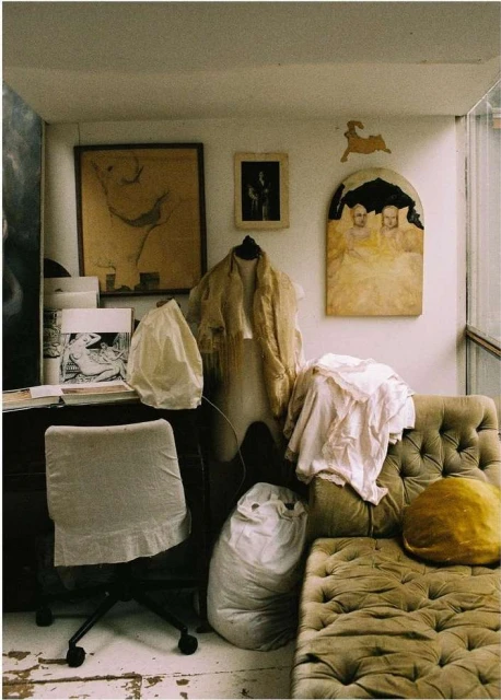 Interior of an artist's studio featuring an antique couch, art pieces, and a dress form draped with fabric, creating a creative atmosphere.