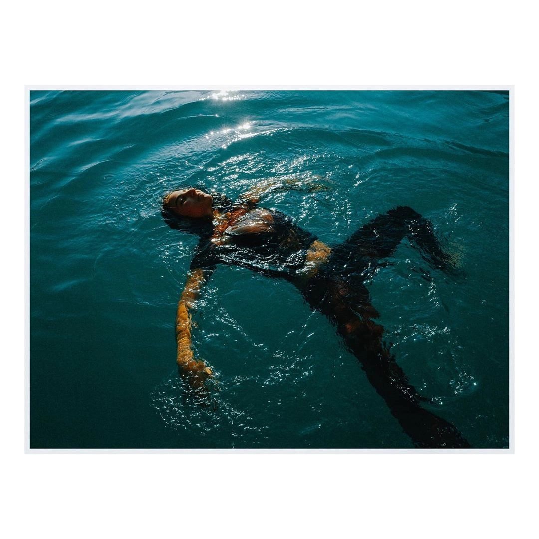 Person floating on their back in clear blue water with sunlight glinting on the surface