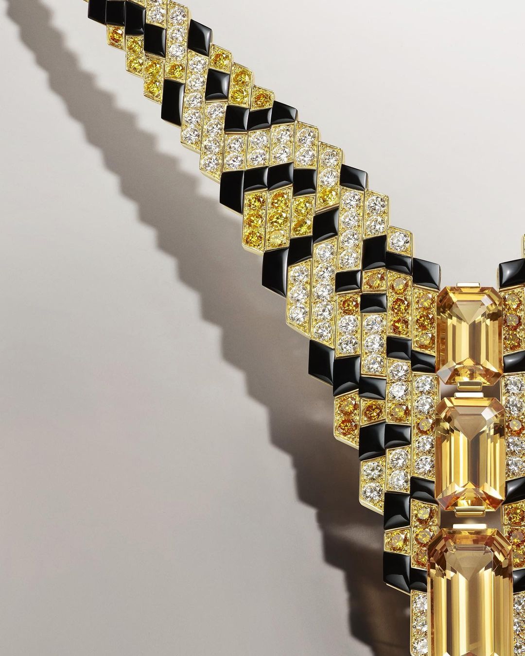 Necklace featuring yellow and white diamonds and black enamel in a geometric pattern against a neutral background, jewelry photography.