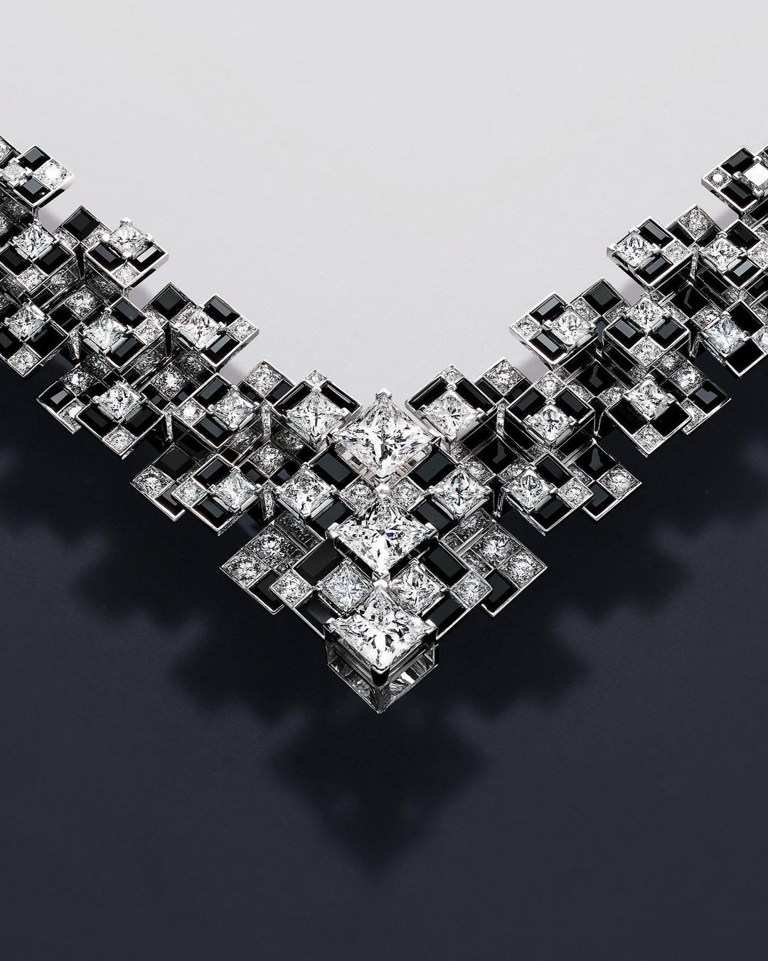 Close-up of a diamond and black gemstone necklace featuring a geometric square design set against a two-tone gradient backdrop.