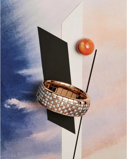 Still life shot of a rose gold ring with inset stones, positioned on a background with geometric shapes and an orange sphere.