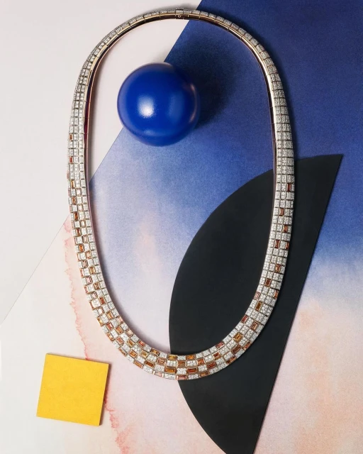Elegant gold necklace with gemstones on a modern blue geometric background, showcased with a blue sphere and a yellow square block.